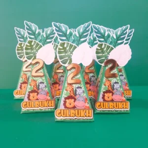 Jungle-themed party favor boxes with tropical leaf designs, a gold number 2, and personalized name tags displayed on a green background.